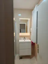 Baño con plato de ducha, cortina blanca y lavabo con espejo retroiluminado sobre mueble de dos cajones